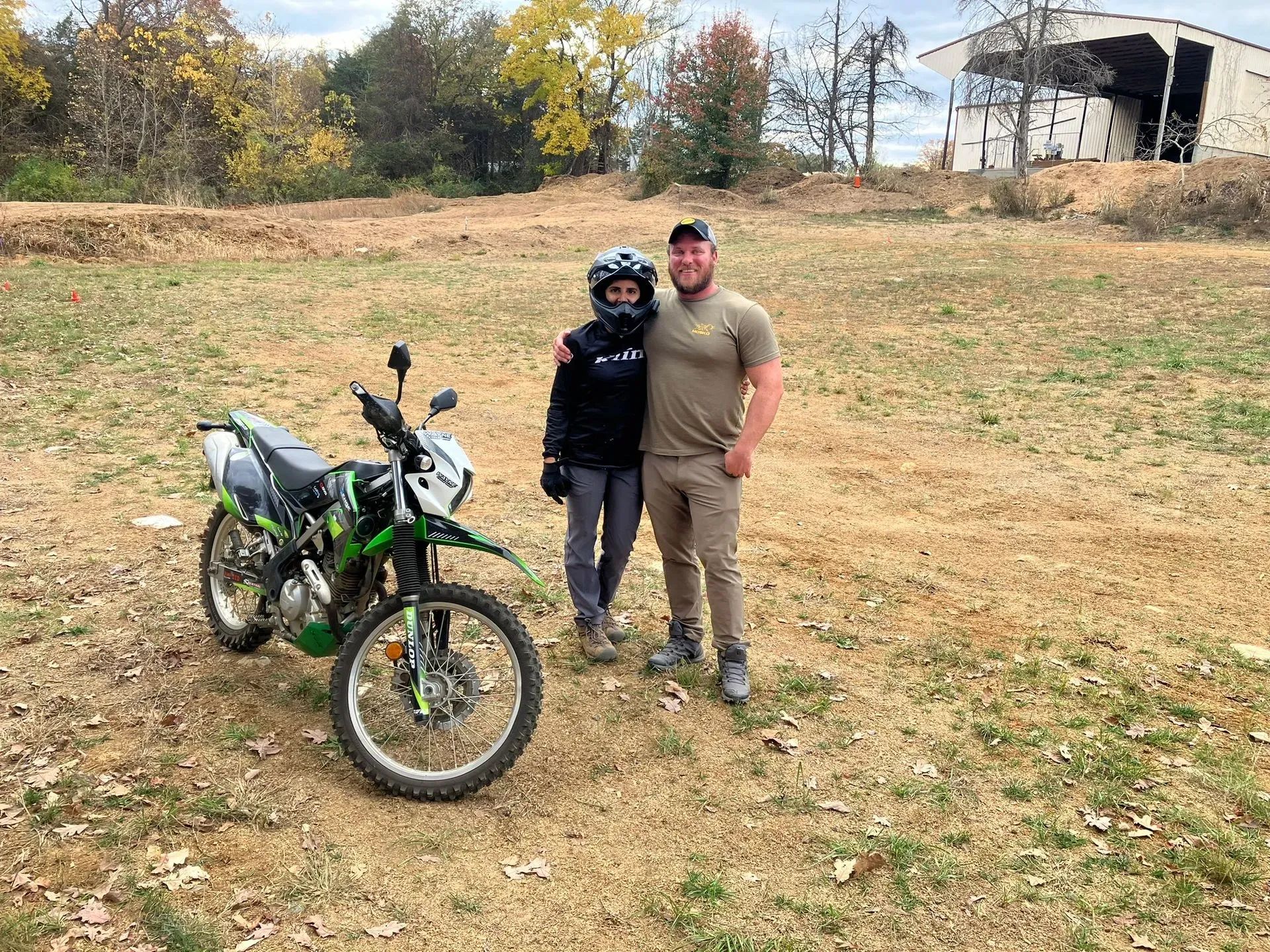 A man and a woman are standing next to a dirt bike in a field