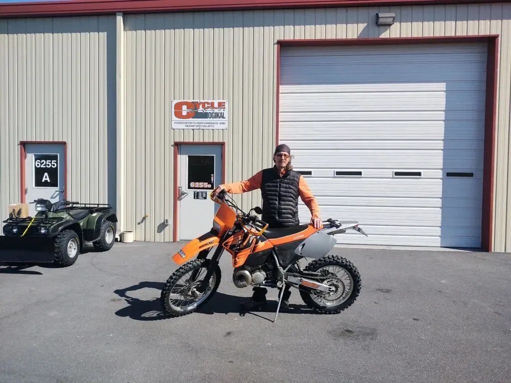 A man is standing next to an orange dirt bike in front of a garage door
