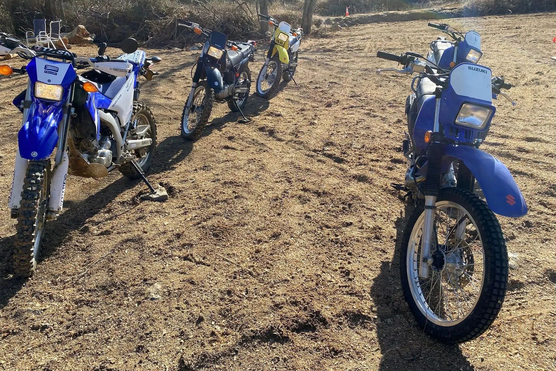 A row of dirt bikes are parked in a dirt field