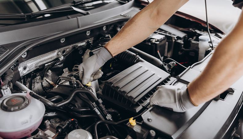 A mechanic in gray gloves working on a car engine under the hood.