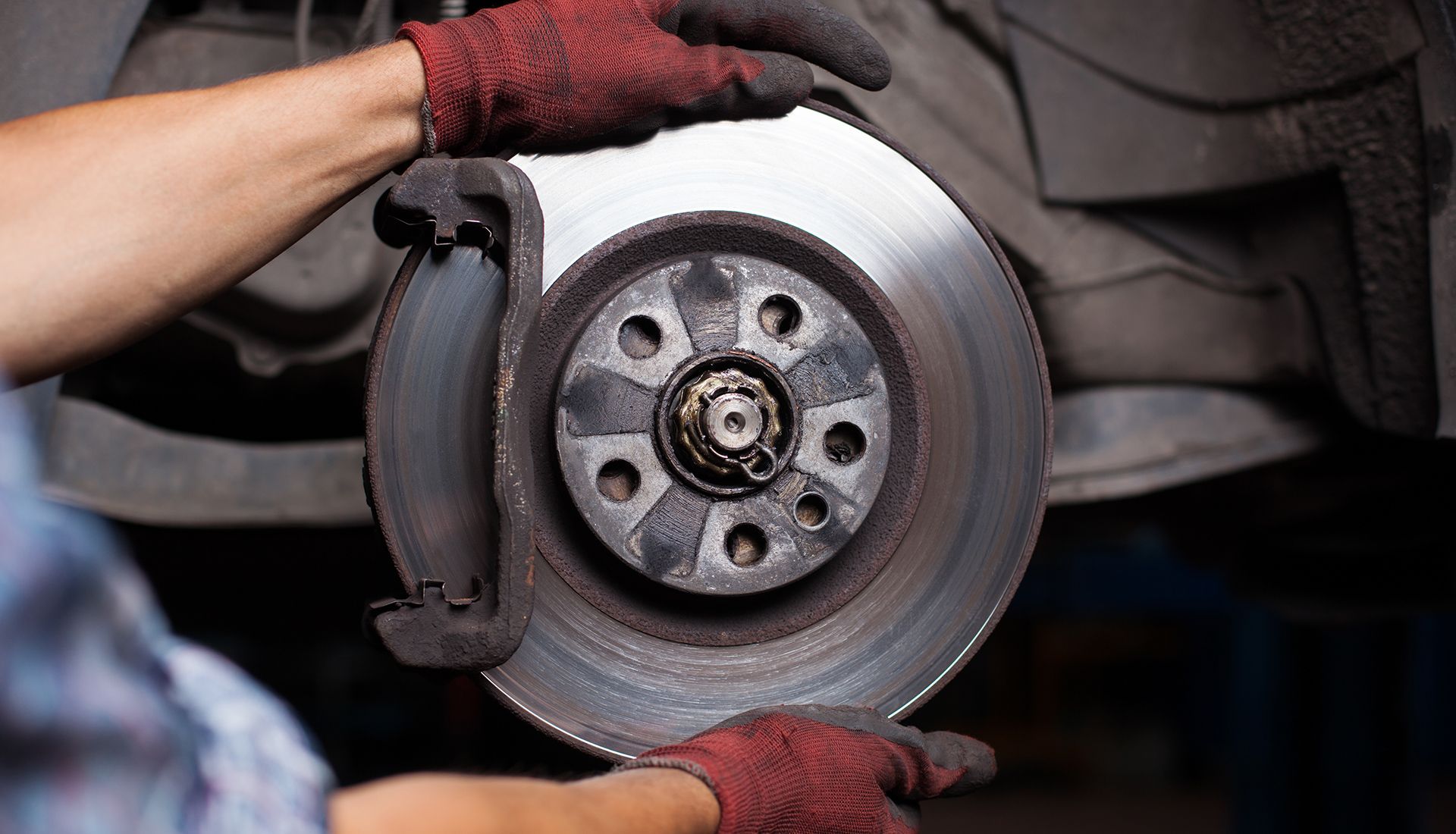 Hands in red gloves holding a car brake rotor, likely during a repair.