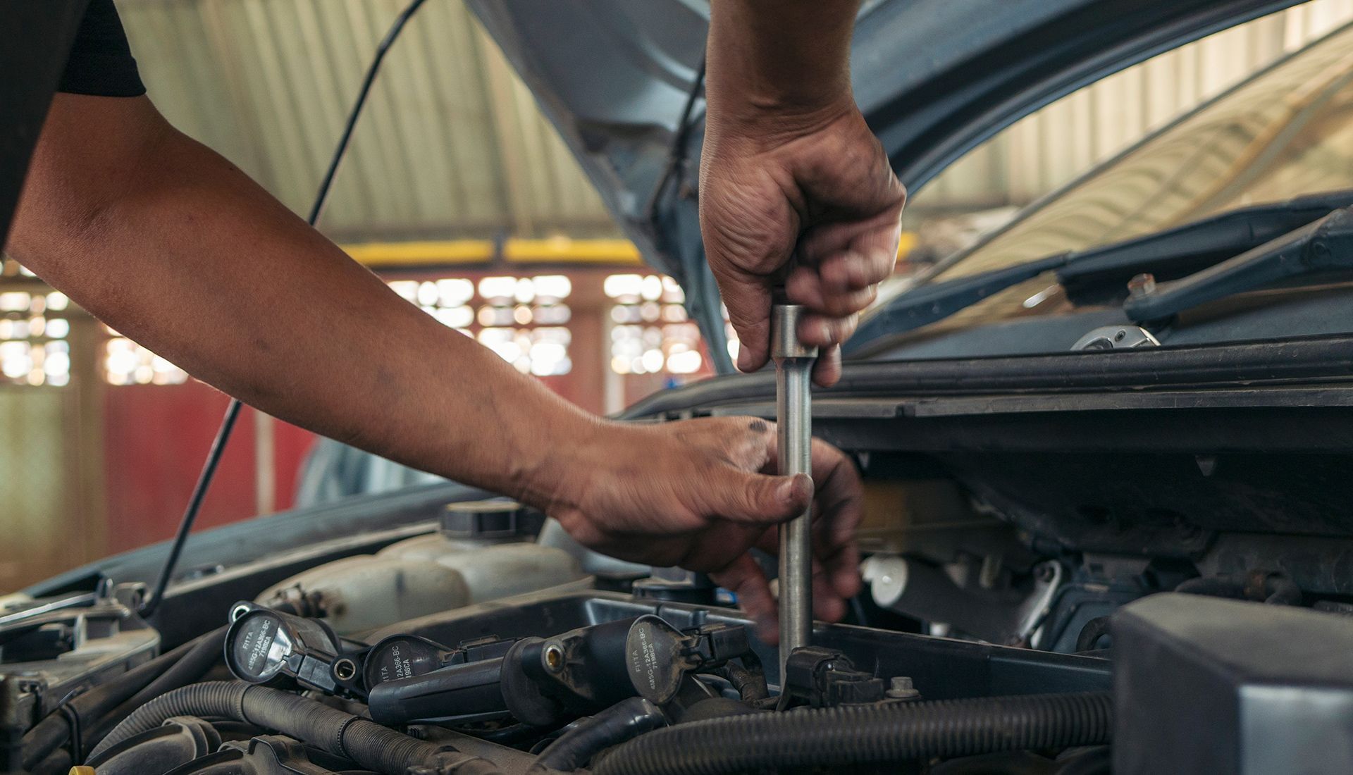 Mechanic using a wrench to work on a car engine with the hood open.