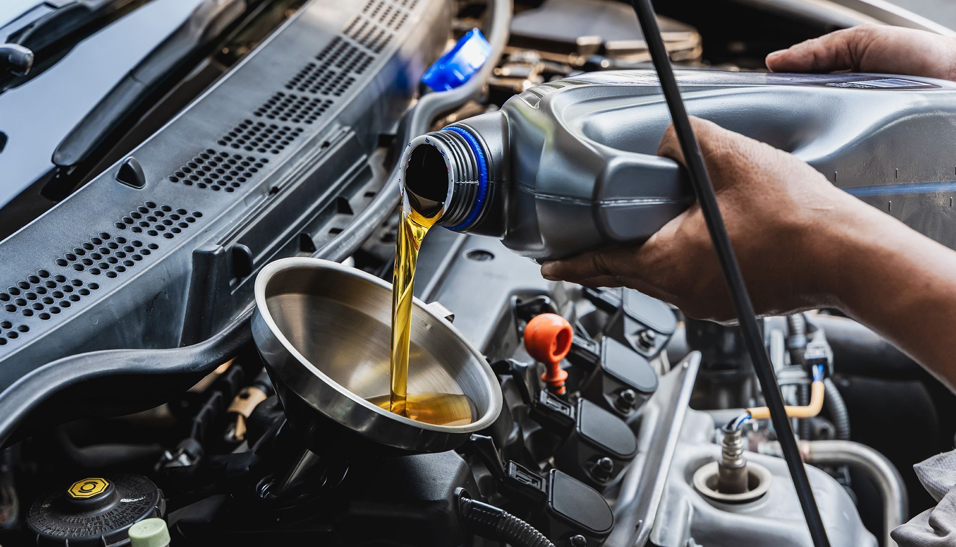 A person pouring oil into a car engine, using a funnel. The oil is golden in color.
