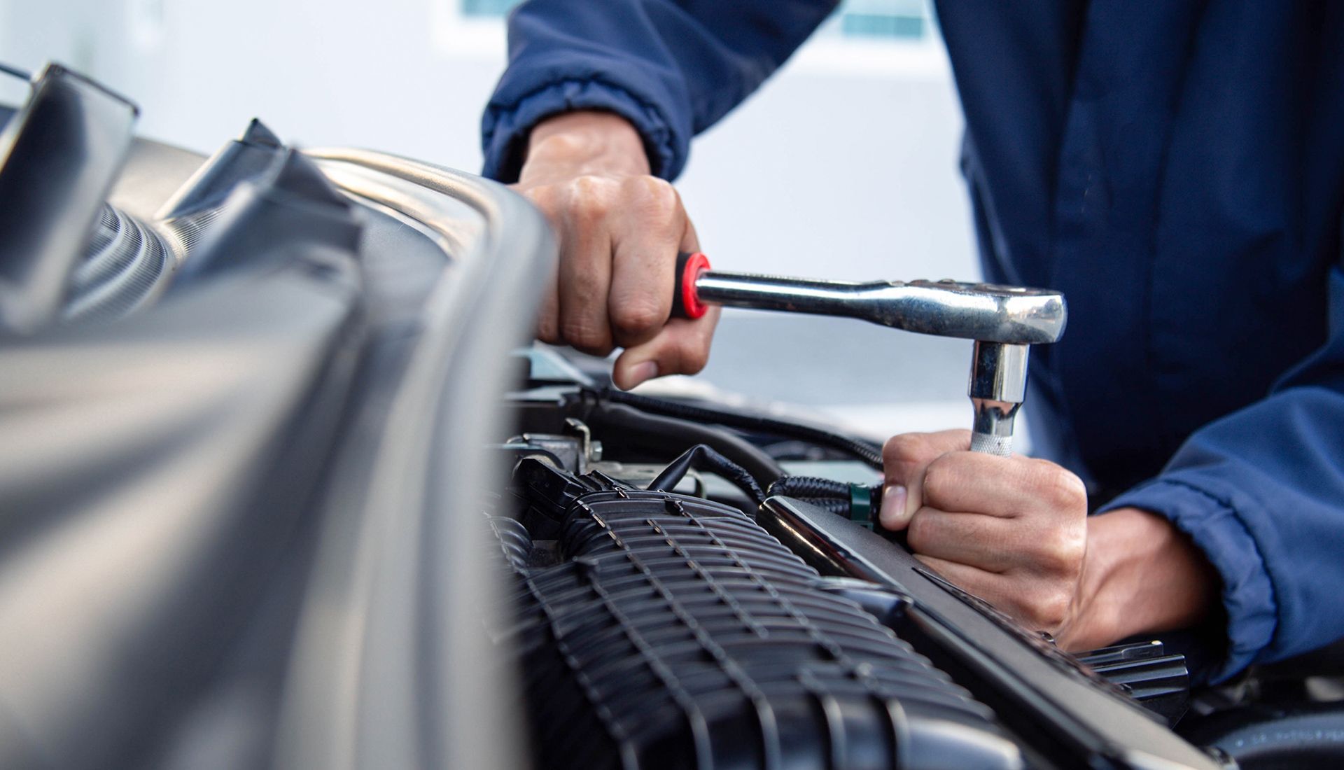 Mechanic in blue uniform working on a car engine, using a wrench.