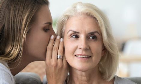A woman is whispering a secret into an older woman 's ear.
