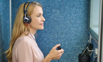 A woman wearing headphones is sitting in a booth.
