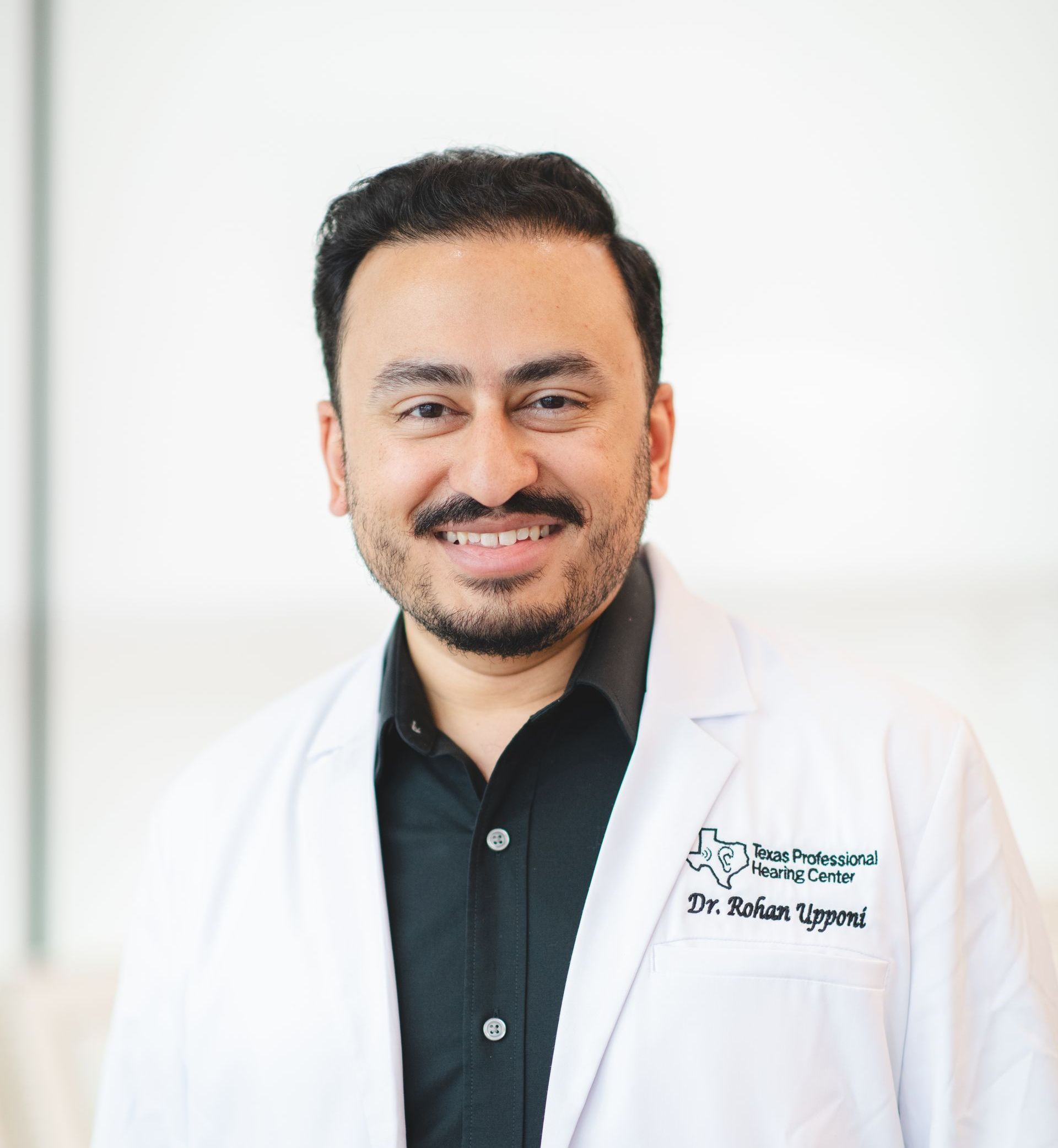 A man with a beard is wearing a white lab coat and smiling