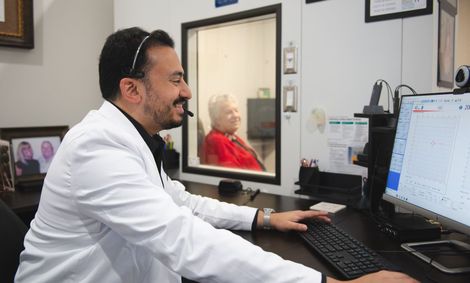 A man in a lab coat is sitting at a desk in front of a computer.