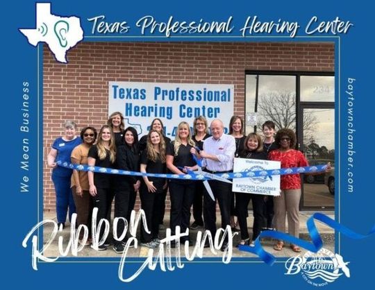 A group of people cutting a blue ribbon in front of texas professional hearing center