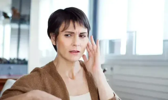 A woman is holding her ear because she has a toothache.