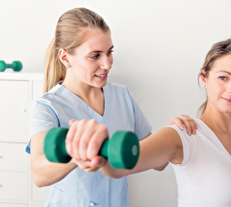 A Nurse Is Helping A Woman Lift A Green Dumbbell — Mark Coulton Cardiff Physiotherapy Centre In Cardiff, NSW