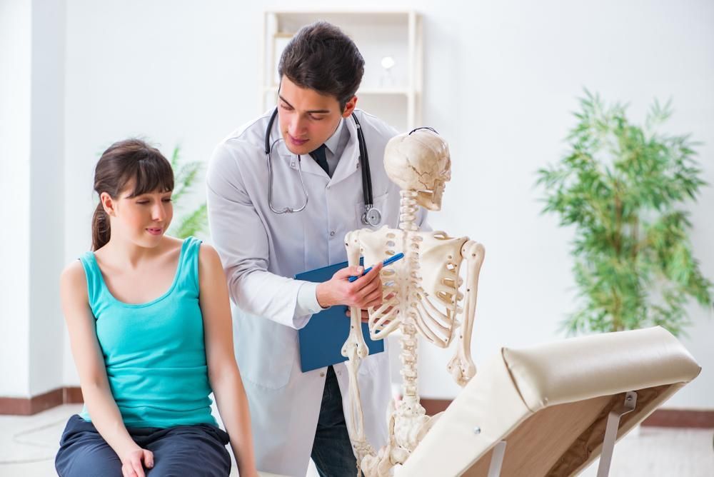 A Doctor Is Talking To A Patient While Looking At A Skeleton — Mark Coulton Cardiff Physiotherapy Centre In Edgeworth, NSW
