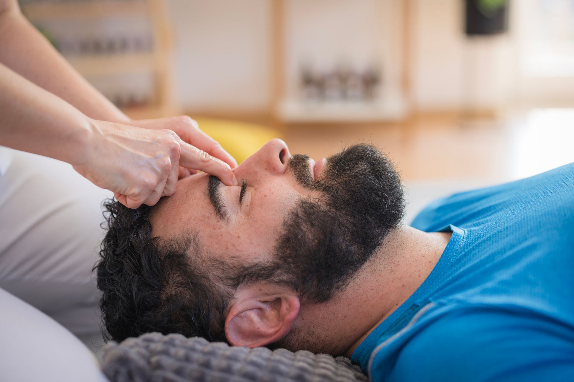 A man with a beard is getting a head massage from a woman.