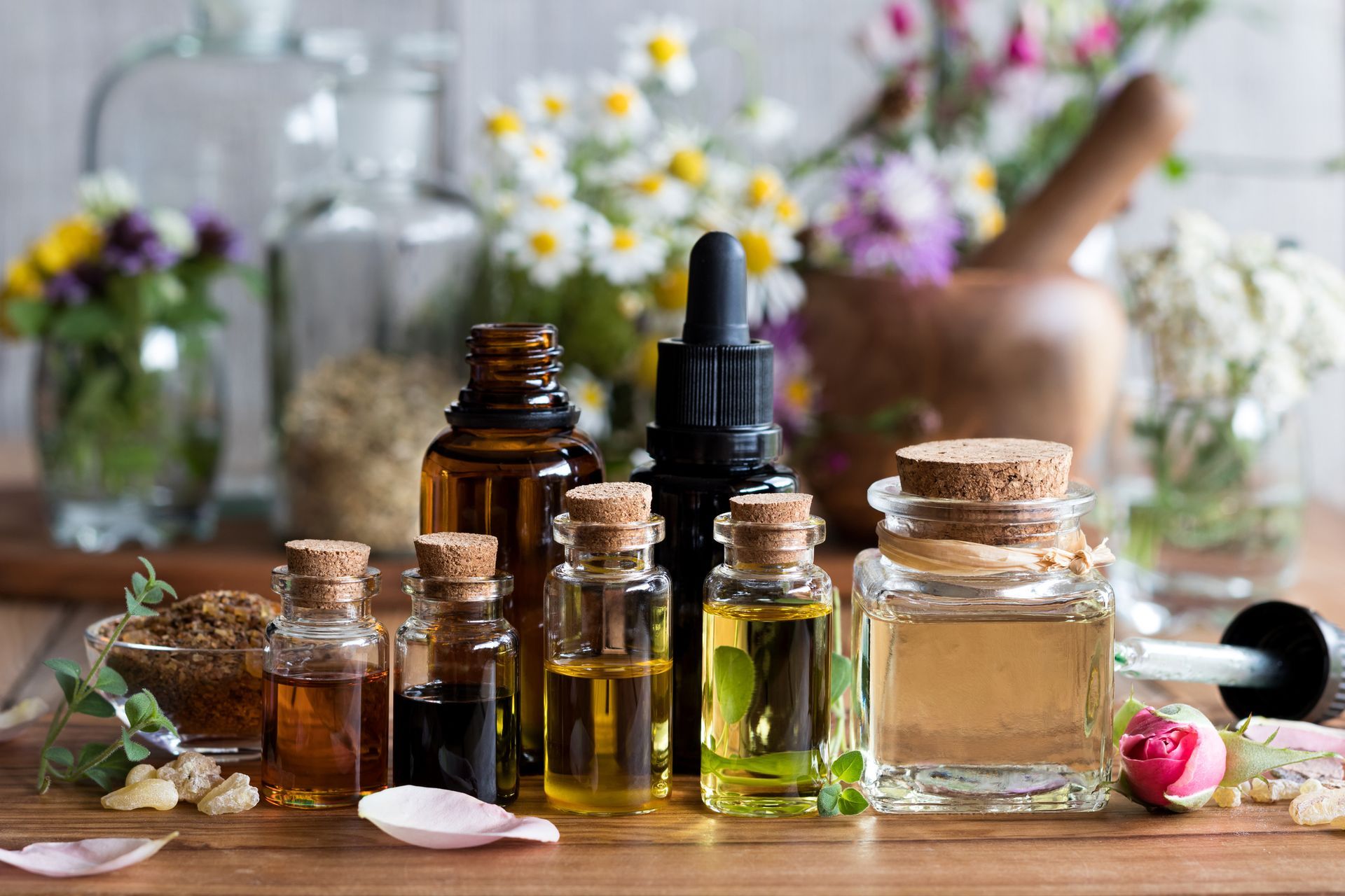 A wooden table topped with bottles of essential oils and flowers.