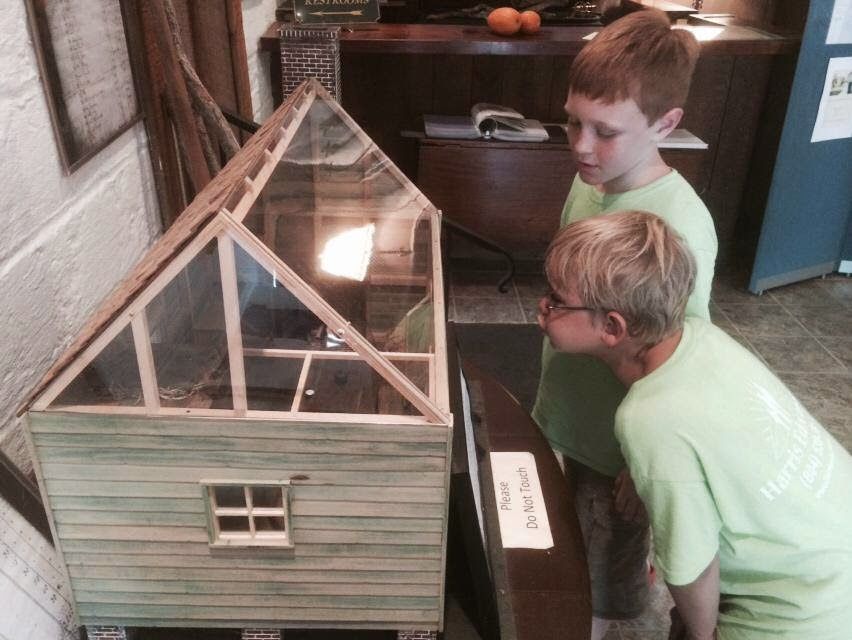 Two boys in green shirts are looking at a model house
