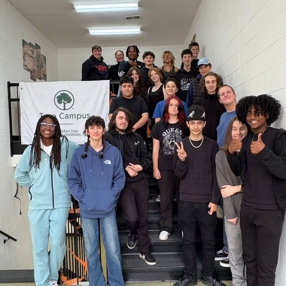Group of students on stairs in a building; some look at camera, smiling. Banner reads 