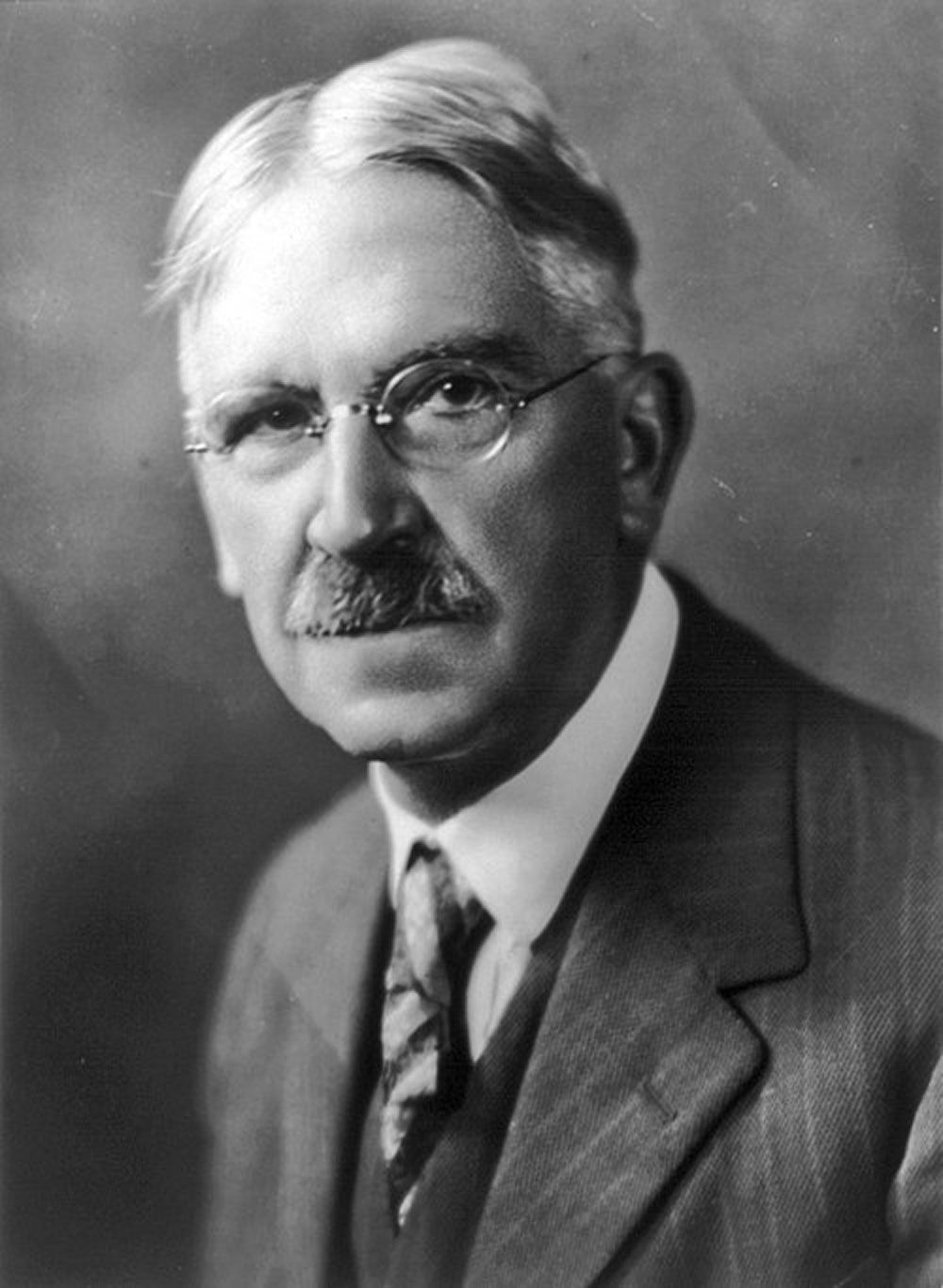 A man with glasses and a mustache is wearing a suit and tie.