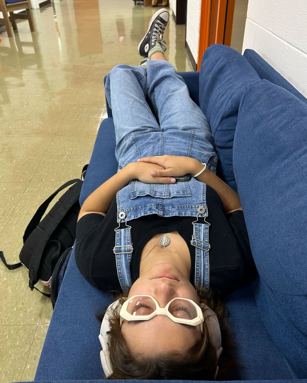 A woman is laying on a blue couch wearing overalls and sunglasses