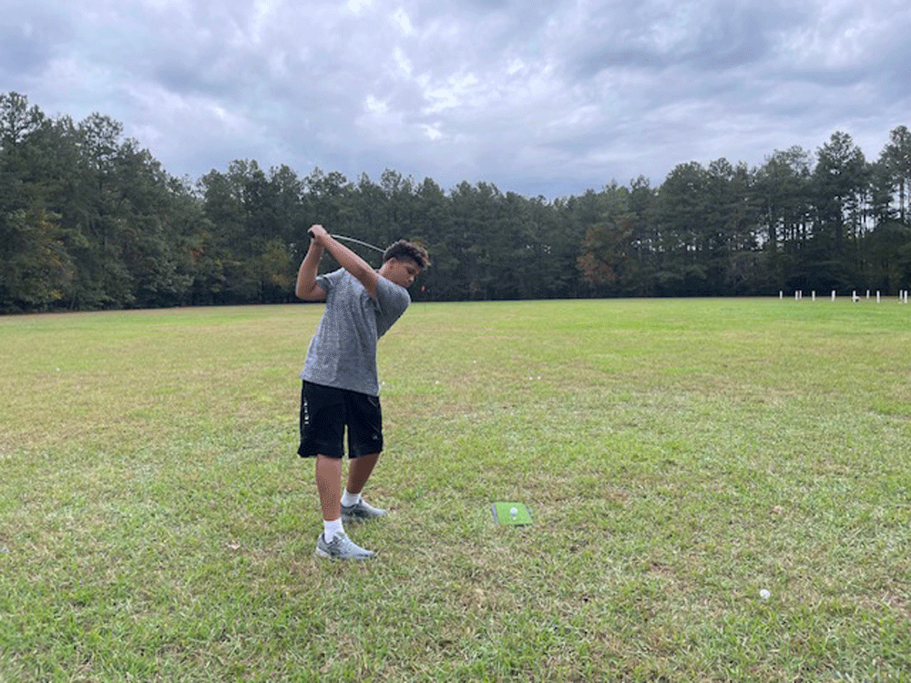 A young man is swinging a golf club in a field.