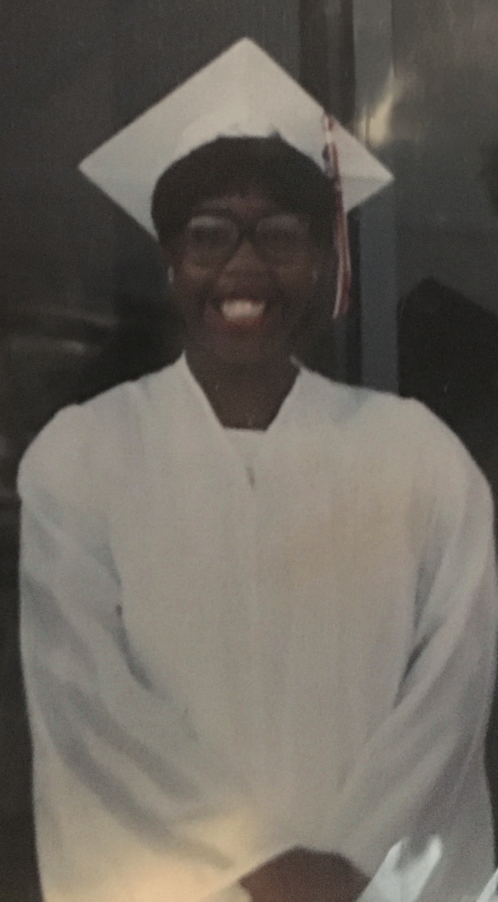 A man wearing a graduation cap and gown is smiling for the camera.