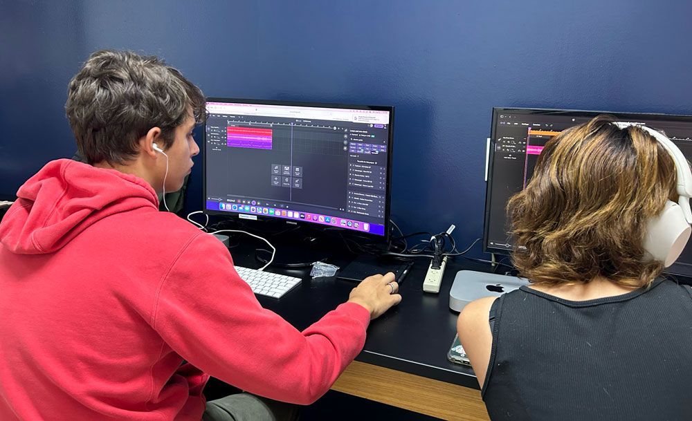 A man and a woman are sitting in front of two computer monitors.