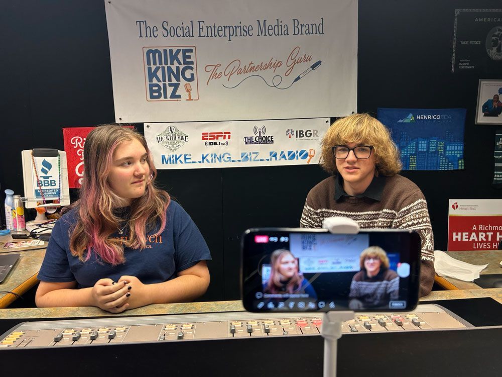 A man and a woman are sitting at a table in front of a mike king biz sign.