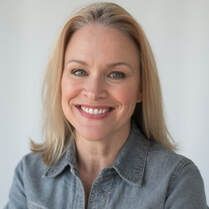 A woman in a denim shirt is smiling for the camera.