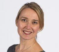 A woman is smiling for the camera and wearing a gray shirt.