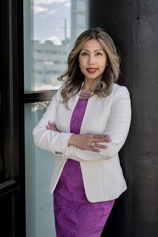 A woman is sitting at a desk with a laptop and a vase of flowers.