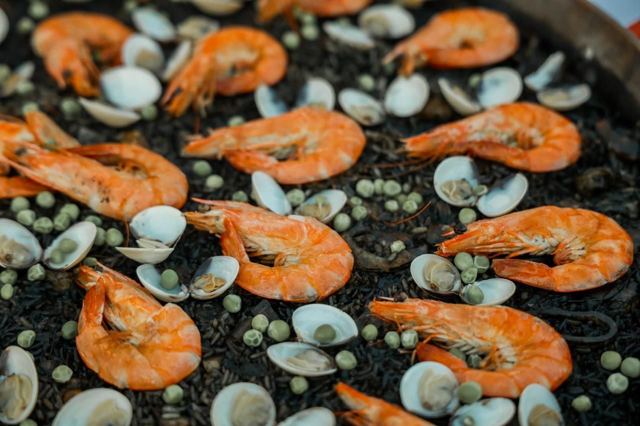 Plato de arroz negro con camarones a la parrilla, almejas y guisantes.