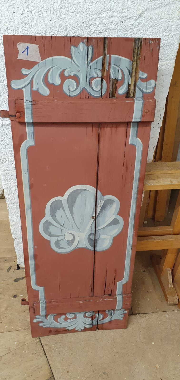 Neben einer Holzleiter befindet sich eine rote Holztür mit einem weissen Muster.