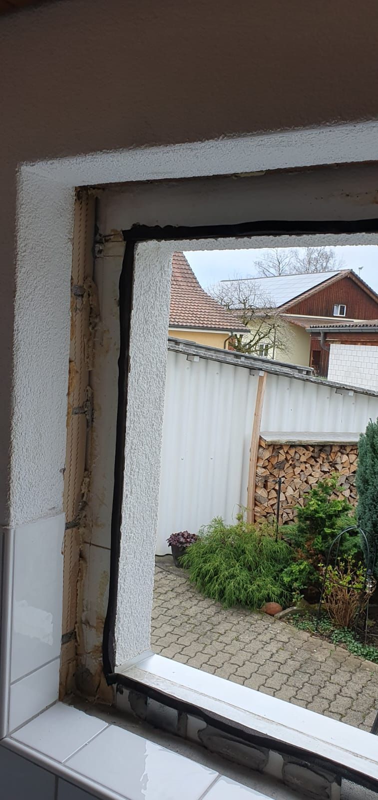 Ein Fenster mit Blick auf einen Hinterhof und einen Zaun.
