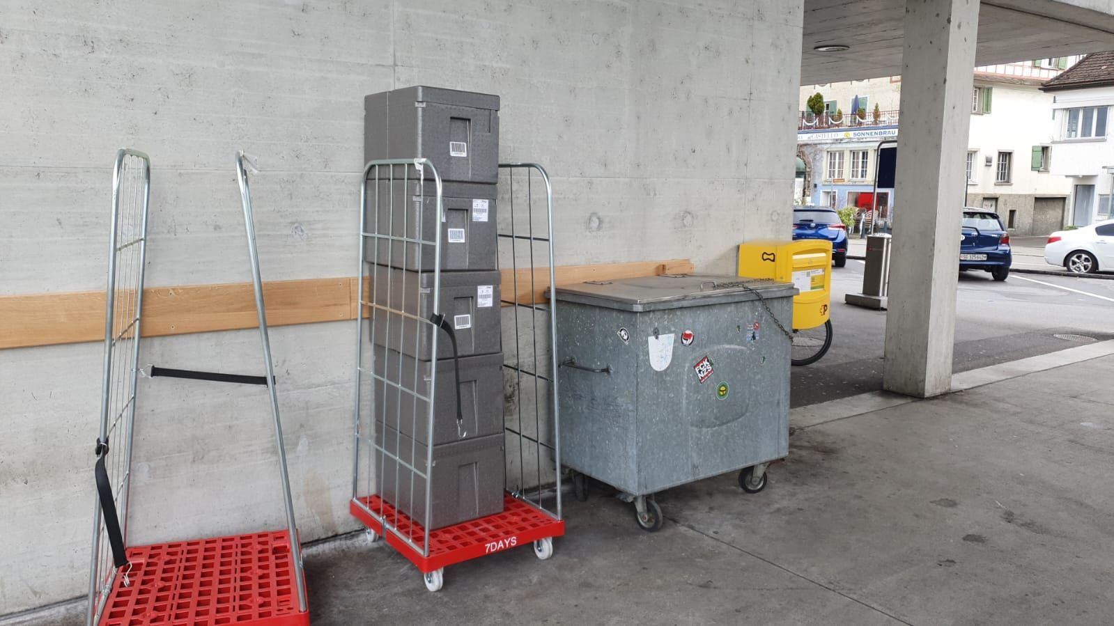 Ein Stapel Kartons steht auf einem Karren neben einer Mülltonne.