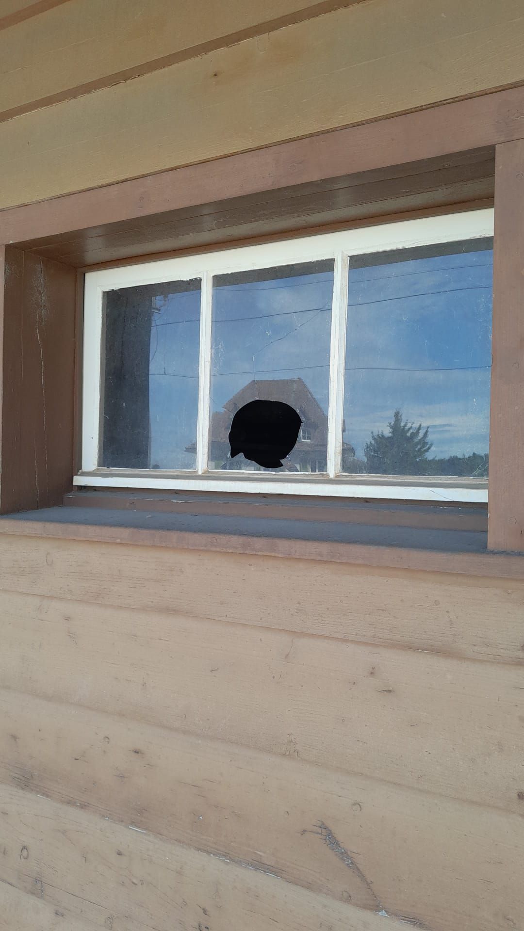 Ein zerbrochenes Fenster an einem Holzgebäude mit einem Loch darin.