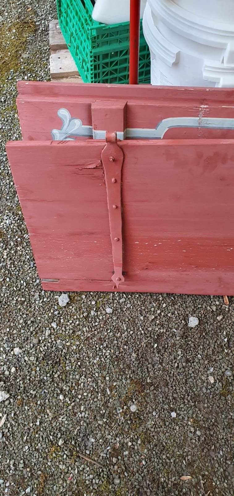 Ein roter Fensterladen steht auf einer Schotterstrasse.