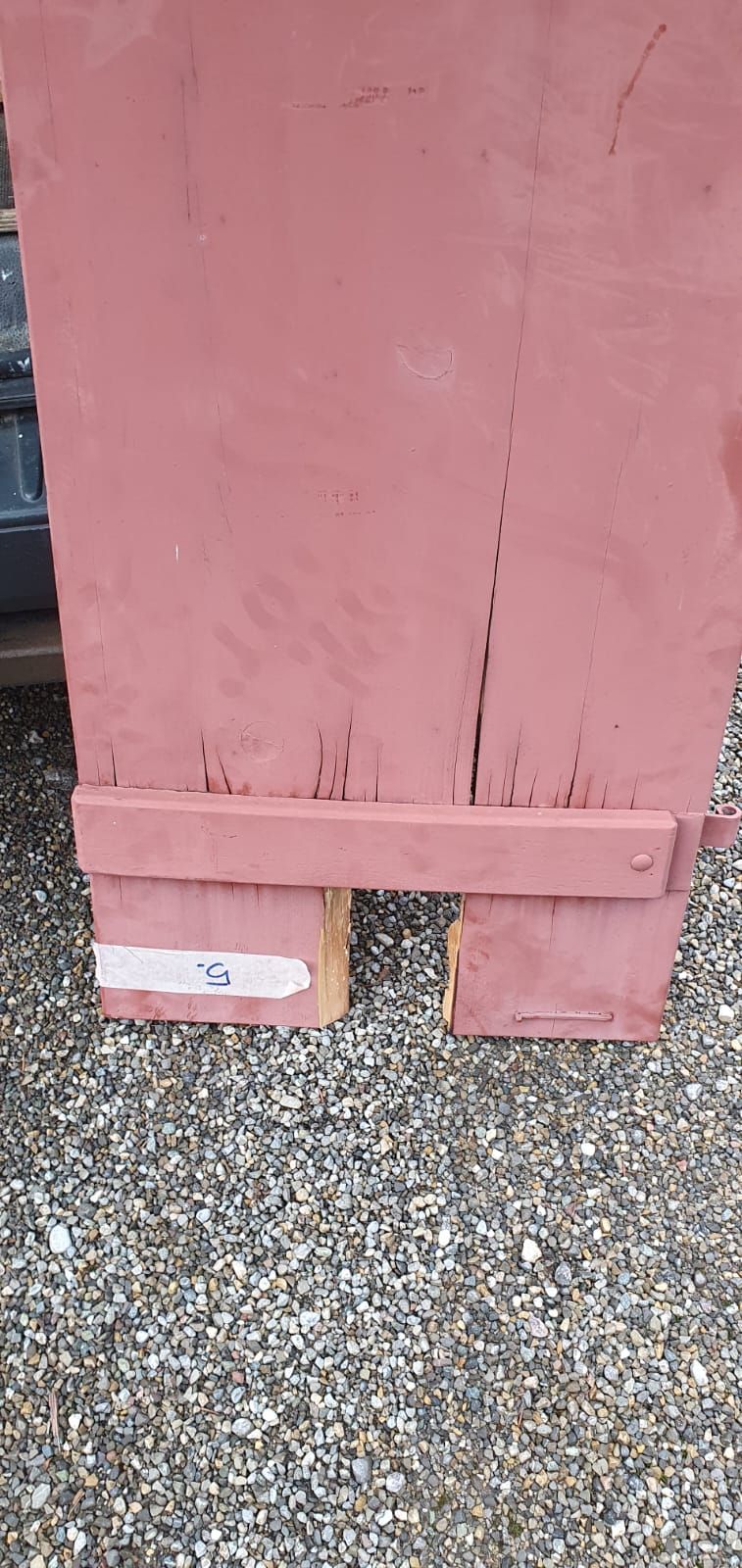 Auf einer Schotterstrasse steht ein roter Fensterladen mit einem Loch darin.