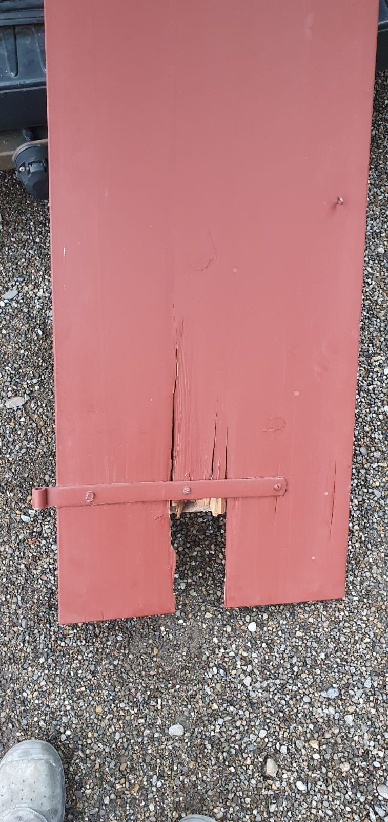 Auf einer Schotterstrasse steht ein roter Fensterladen mit einem Loch darin.