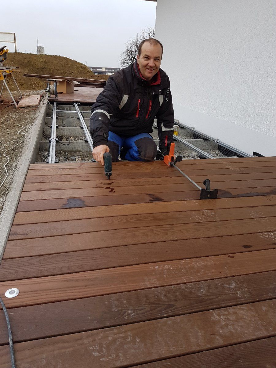 Ein Mann arbeitet mit einer Bohrmaschine auf einem Holzdeck.