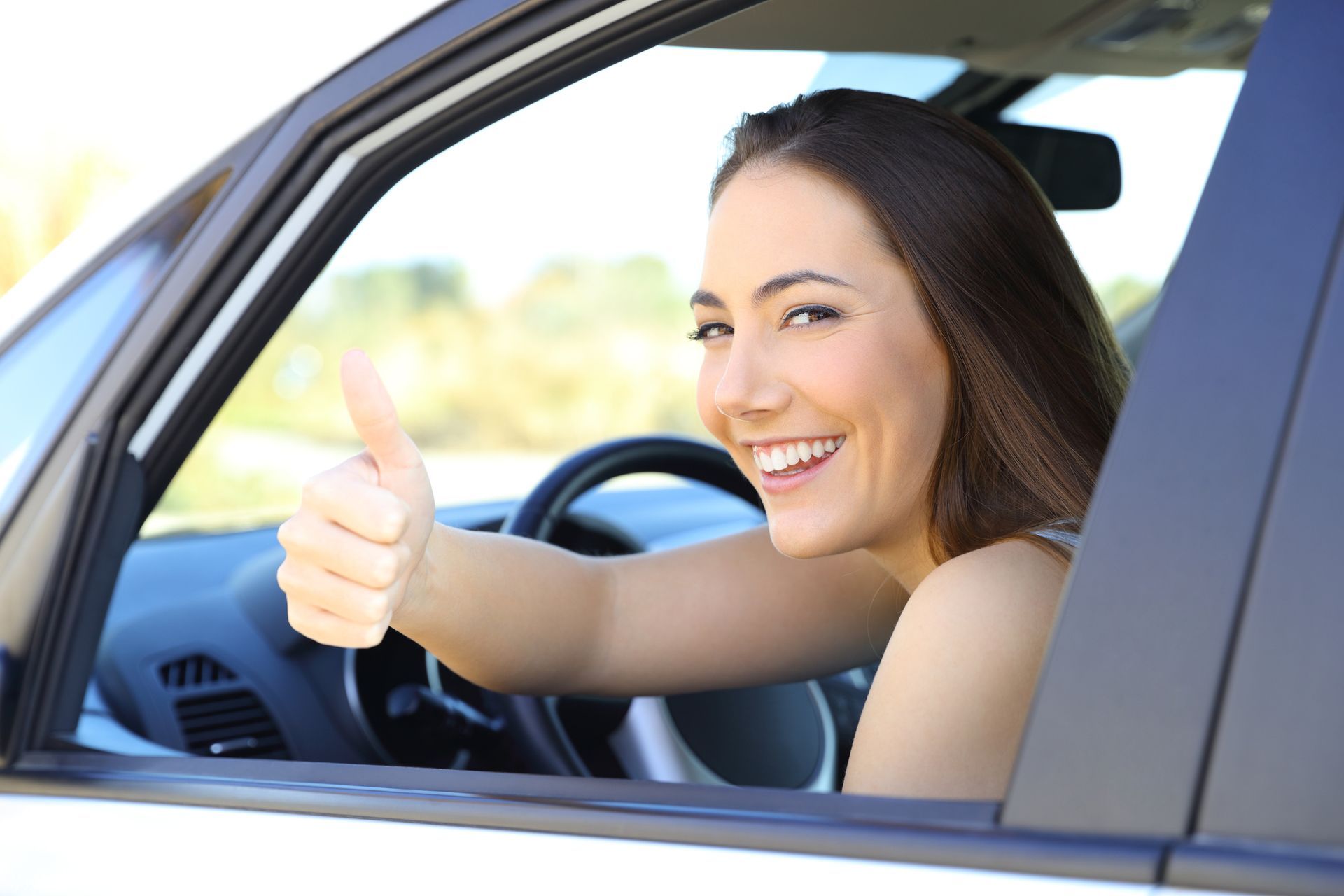 A woman is giving a thumbs up while sitting in a car.