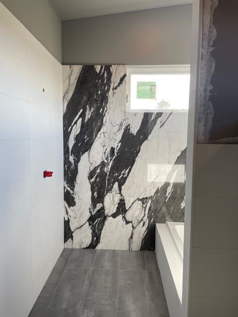 Bathroom with a black and white marble accent wall, a small window, and a gray floor.