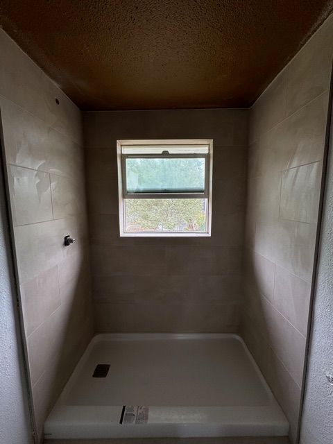 Shower stall with a window, light gray tile walls, and a white shower base.