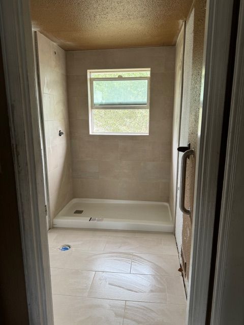 Bathroom with shower, tan tile, window, and white shower base. Viewed from doorway.