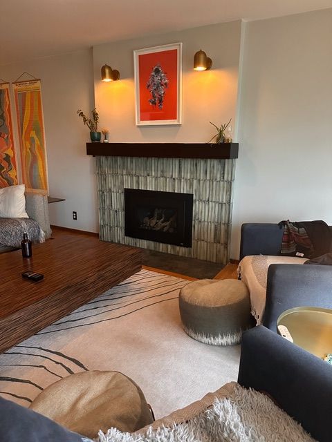 Living room with fireplace, art, and furniture; fireplace has stacked tile and dark wood mantel.