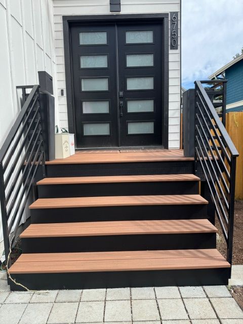 Exterior view: black double doors and stairs leading up. Black railings, composite stairs in brown and black.