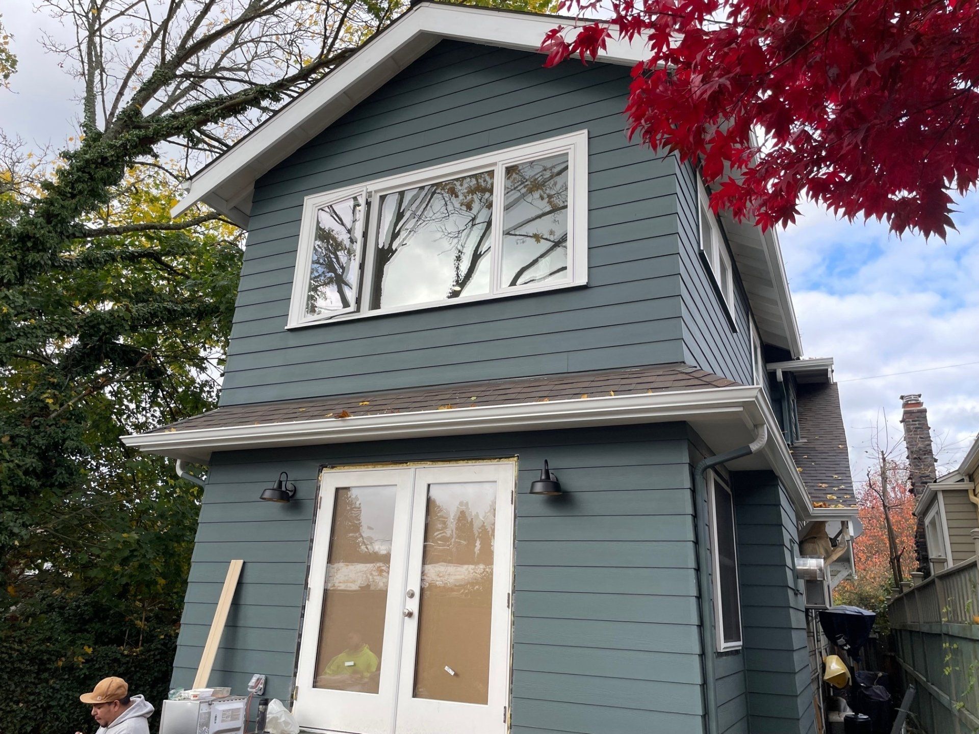 Two-story house with blue siding, white trim, and a red-leaved tree.