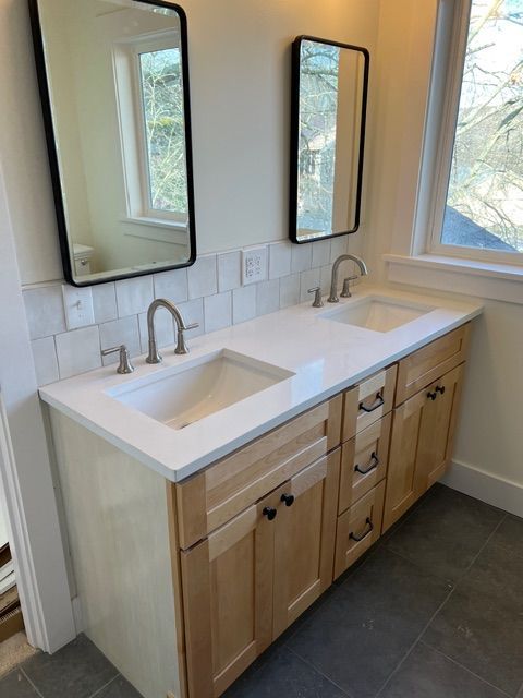 Double sink vanity with light wood cabinets, white countertop, and black framed mirrors.