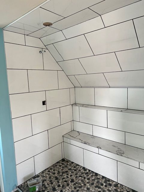 White tiled shower with black grout, built-in bench, and pebble floor.