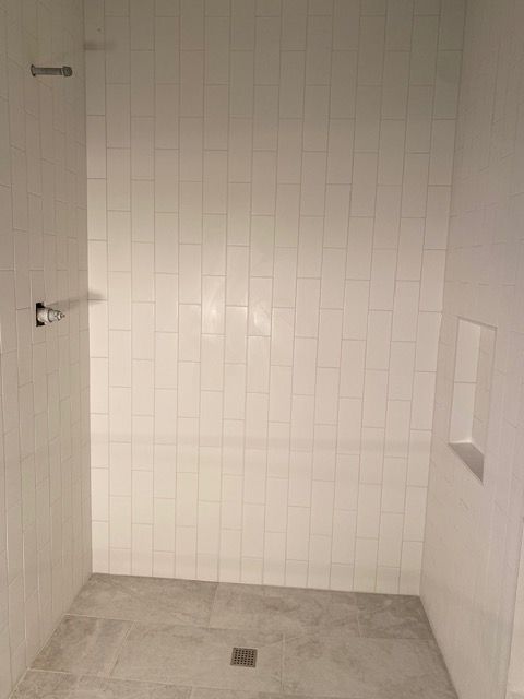 White tiled shower with built-in shelf and shower fixtures; light gray floor.