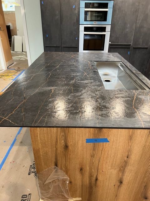 Kitchen island with dark countertop and wood base, stainless steel sink. Construction in progress.