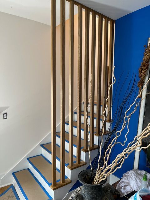 Staircase with wooden vertical railing, tan steps and white risers, blue painter's tape, blue and beige walls.